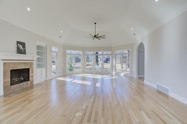 unfurnished living room with a tiled fireplace, light hardwood / wood-style floors, ceiling fan, ornamental molding, and built in shelves