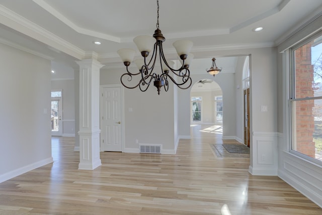 unfurnished dining area with an inviting chandelier, decorative columns, a raised ceiling, light hardwood / wood-style floors, and ornamental molding