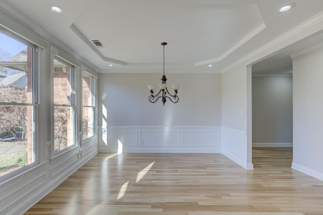 empty room with a tray ceiling, light hardwood / wood-style floors, and an inviting chandelier