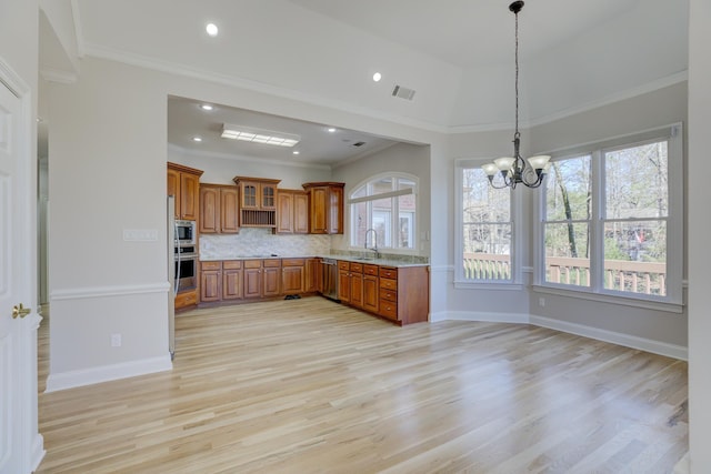 kitchen with appliances with stainless steel finishes, backsplash, a notable chandelier, sink, and light hardwood / wood-style flooring