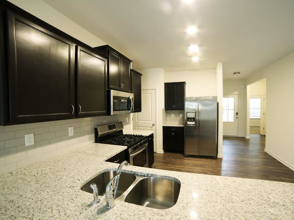 kitchen featuring backsplash, light stone counters, appliances with stainless steel finishes, and dark hardwood / wood-style flooring