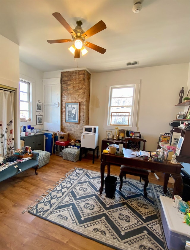 office space featuring brick wall, a healthy amount of sunlight, ceiling fan, and hardwood / wood-style flooring