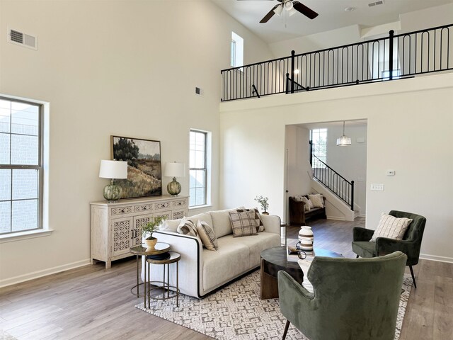 living room with a towering ceiling, ceiling fan, and light wood-type flooring