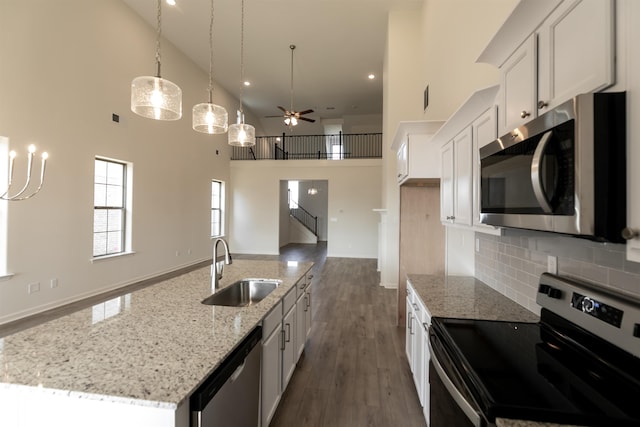 kitchen with appliances with stainless steel finishes, sink, white cabinets, hanging light fixtures, and a kitchen island with sink