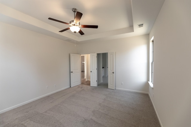 unfurnished bedroom featuring light colored carpet, a raised ceiling, and ceiling fan