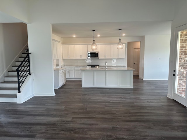 kitchen with appliances with stainless steel finishes, hanging light fixtures, white cabinets, dark hardwood / wood-style flooring, and a center island with sink