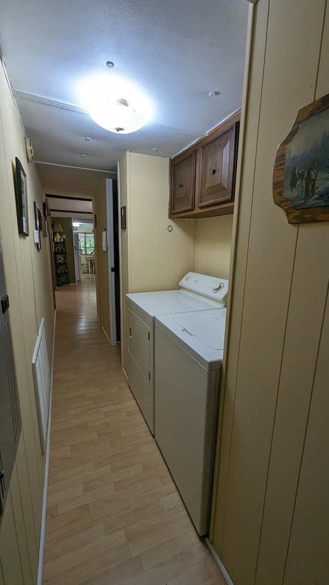 clothes washing area with washing machine and dryer, light wood-type flooring, and cabinets