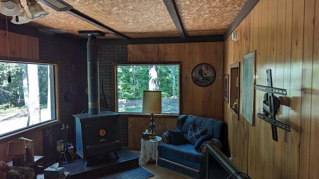 sitting room with wood walls, brick wall, ceiling fan, and a wood stove