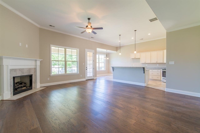 unfurnished living room with ceiling fan, a tiled fireplace, ornamental molding, and dark hardwood / wood-style flooring