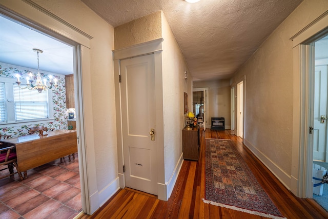 hall with an inviting chandelier, dark hardwood / wood-style flooring, and a textured ceiling