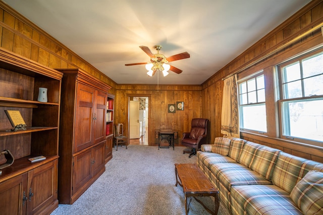 sitting room featuring ceiling fan, light colored carpet, and wood walls