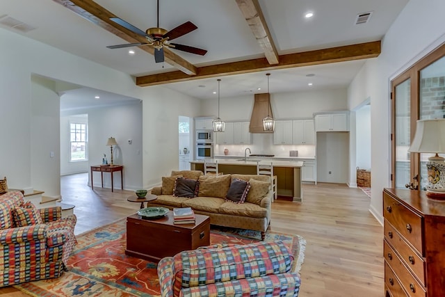 living room featuring beam ceiling, ceiling fan, sink, and light wood-type flooring