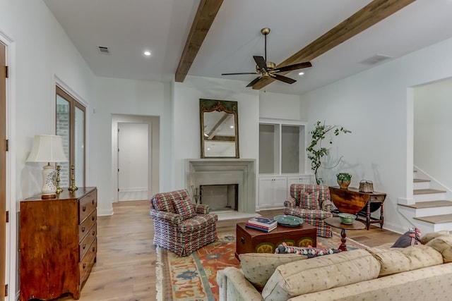 living room featuring beamed ceiling, ceiling fan, and light wood-type flooring