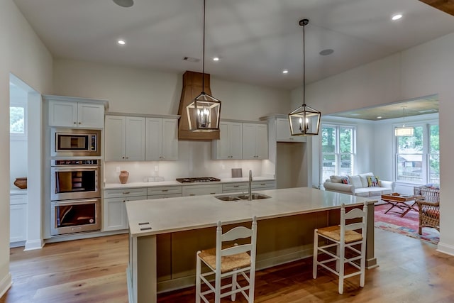 kitchen featuring appliances with stainless steel finishes, light hardwood / wood-style flooring, sink, and a center island with sink