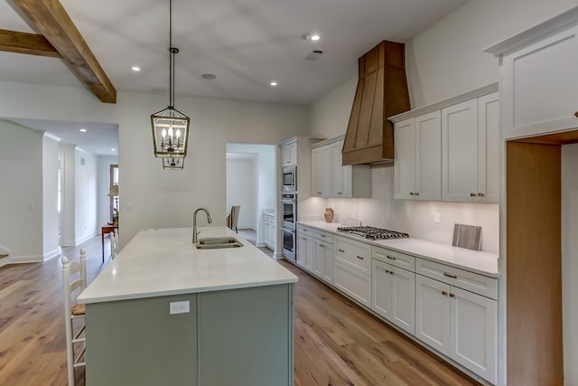 kitchen with white cabinets, light hardwood / wood-style flooring, hanging light fixtures, and a kitchen island with sink