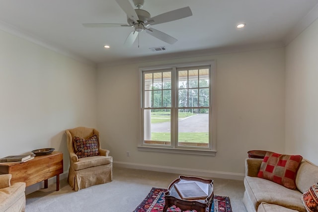 sitting room with ceiling fan, crown molding, and light colored carpet