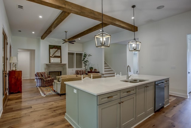 kitchen with pendant lighting, ceiling fan with notable chandelier, light wood-type flooring, and an island with sink