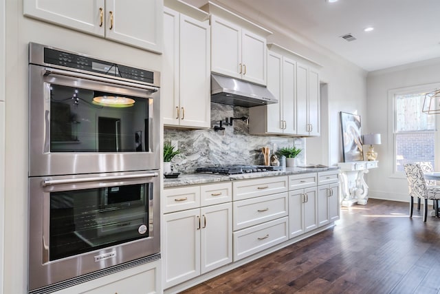 kitchen featuring dark hardwood / wood-style floors, decorative backsplash, light stone countertops, appliances with stainless steel finishes, and white cabinetry