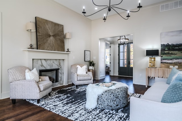 living room featuring crown molding, dark hardwood / wood-style flooring, a high end fireplace, and an inviting chandelier