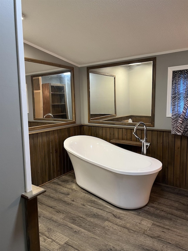 bathroom featuring ornamental molding, a washtub, a textured ceiling, wooden walls, and hardwood / wood-style floors