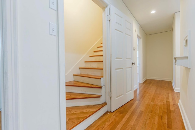 hall featuring light wood-style floors, stairs, baseboards, and recessed lighting