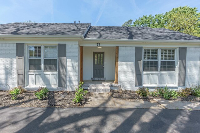 property entrance featuring brick siding and a shingled roof