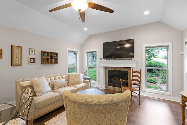 living room with dark wood-type flooring, a tiled fireplace, vaulted ceiling, and ceiling fan