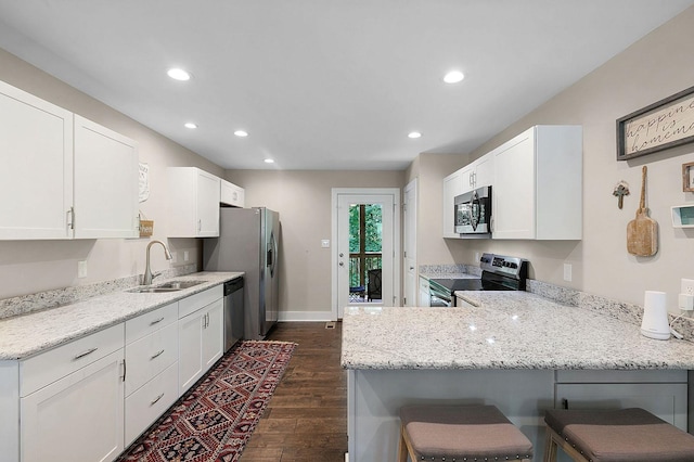 kitchen with kitchen peninsula, dark wood-type flooring, white cabinetry, stainless steel appliances, and a kitchen breakfast bar