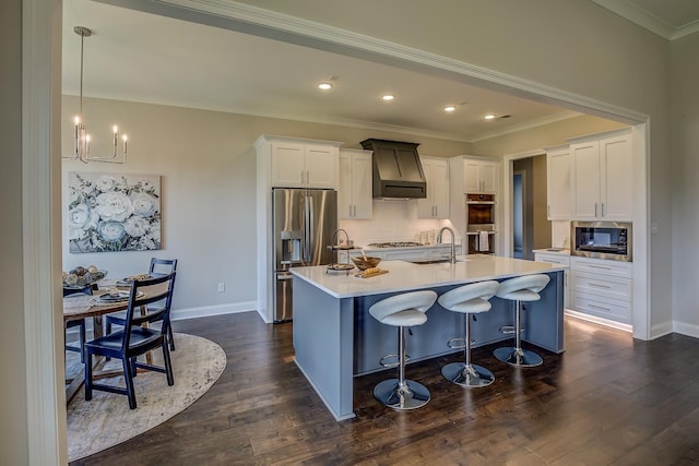 kitchen with premium range hood, decorative light fixtures, a center island with sink, appliances with stainless steel finishes, and white cabinets