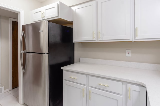 kitchen with stainless steel fridge, white cabinets, light tile floors, and light stone countertops