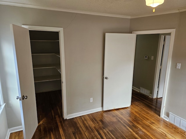 unfurnished bedroom with dark hardwood / wood-style flooring, a textured ceiling, a walk in closet, and a closet