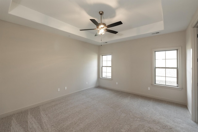 empty room with light carpet, a raised ceiling, and ceiling fan