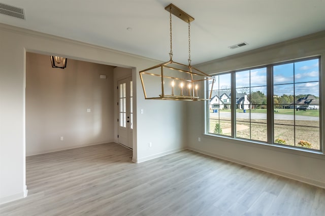 unfurnished dining area with an inviting chandelier, ornamental molding, and light wood-type flooring