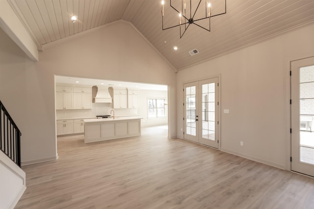 unfurnished living room with light hardwood / wood-style flooring, high vaulted ceiling, french doors, and a chandelier