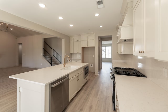 kitchen featuring sink, appliances with stainless steel finishes, a kitchen island with sink, white cabinetry, and light hardwood / wood-style floors