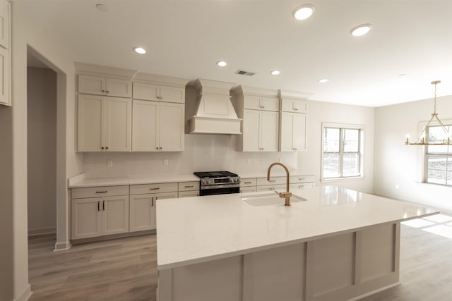 kitchen with gas stove, sink, decorative light fixtures, custom range hood, and a kitchen island with sink