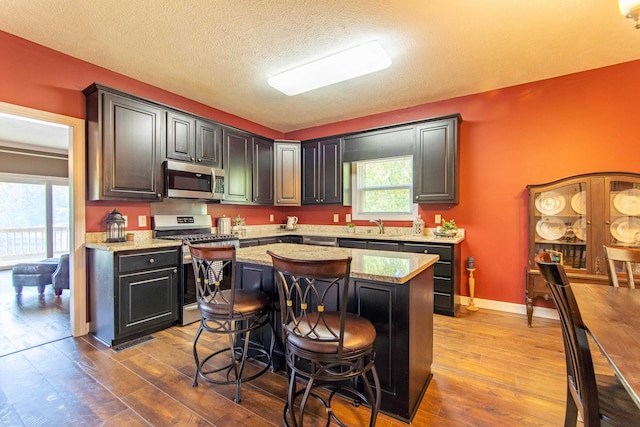 kitchen with a kitchen breakfast bar, stainless steel appliances, wood-type flooring, light stone countertops, and a center island