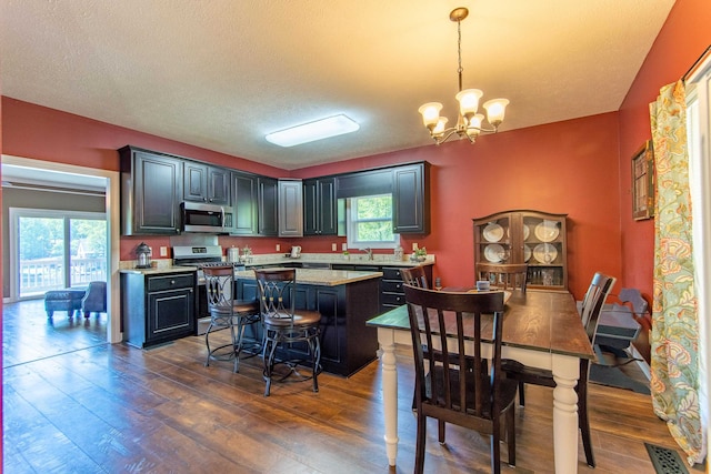 dining space featuring plenty of natural light, a textured ceiling, a notable chandelier, and dark wood-type flooring