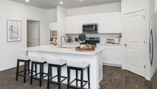 kitchen with white cabinetry, stainless steel appliances, dark hardwood / wood-style flooring, and an island with sink