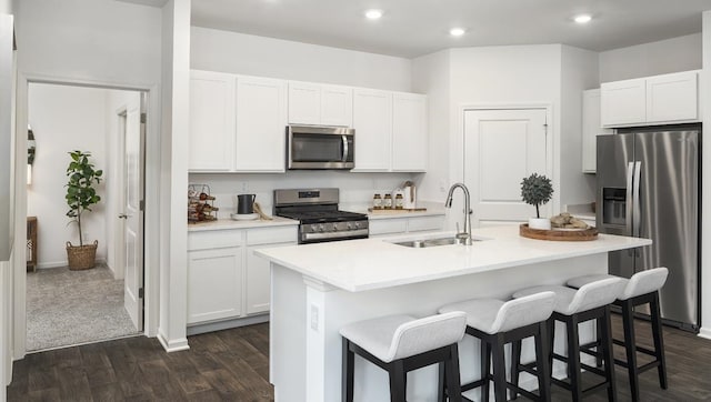 kitchen with stainless steel appliances, white cabinets, sink, a center island with sink, and dark carpet