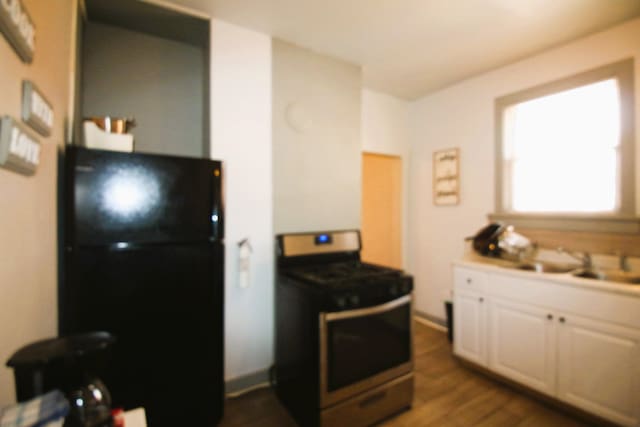 kitchen with stainless steel stove, black refrigerator, white cabinets, dark hardwood / wood-style floors, and sink