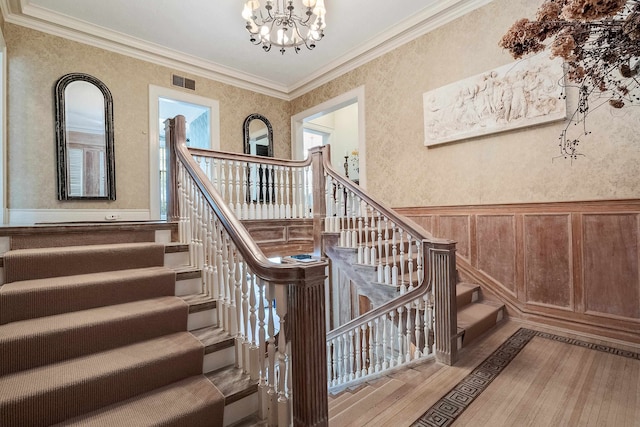 stairs with an inviting chandelier, ornamental molding, and light hardwood / wood-style floors