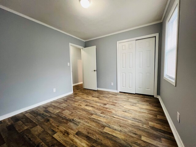 unfurnished bedroom with a closet, dark wood-type flooring, and crown molding