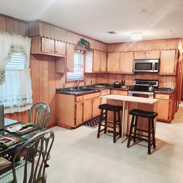 kitchen with light brown cabinetry, sink, stainless steel appliances, light tile flooring, and a kitchen bar