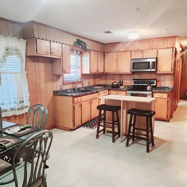 kitchen with appliances with stainless steel finishes, sink, light tile floors, light brown cabinetry, and a breakfast bar area