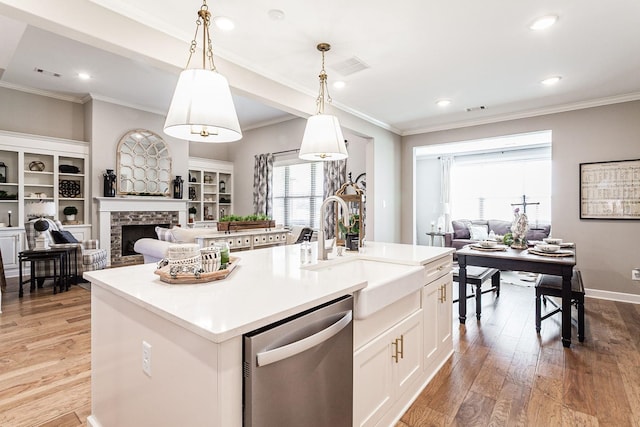 kitchen featuring stainless steel dishwasher, a kitchen island with sink, pendant lighting, light hardwood / wood-style flooring, and a stone fireplace