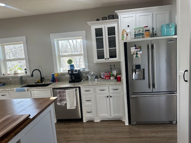 kitchen with stainless steel appliances, white cabinets, sink, and light stone countertops