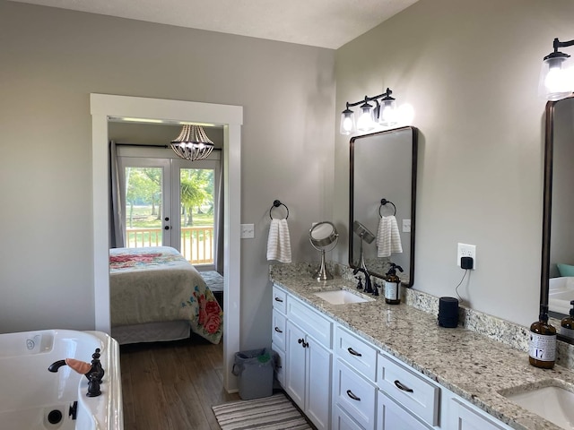 bathroom with double vanity, french doors, hardwood / wood-style floors, a bath, and an inviting chandelier