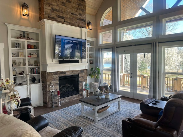 living room featuring french doors, a stone fireplace, a towering ceiling, built in features, and dark hardwood / wood-style flooring