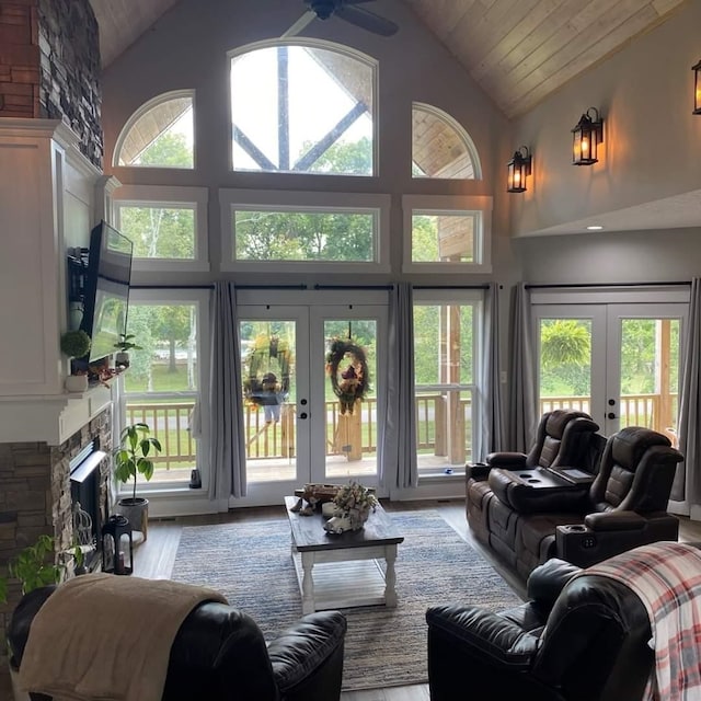 living room with high vaulted ceiling, french doors, light hardwood / wood-style floors, and a stone fireplace